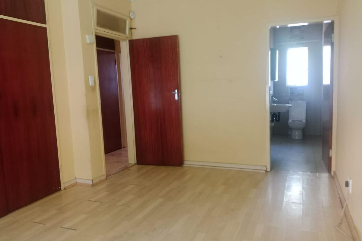 An empty bedroom featuring built-in cupboards, laminate flooring, and direct access to an en-suite bathroom.