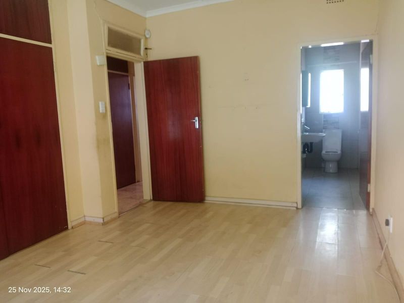 An empty bedroom featuring built-in cupboards, laminate flooring, and direct access to an en-suite bathroom.