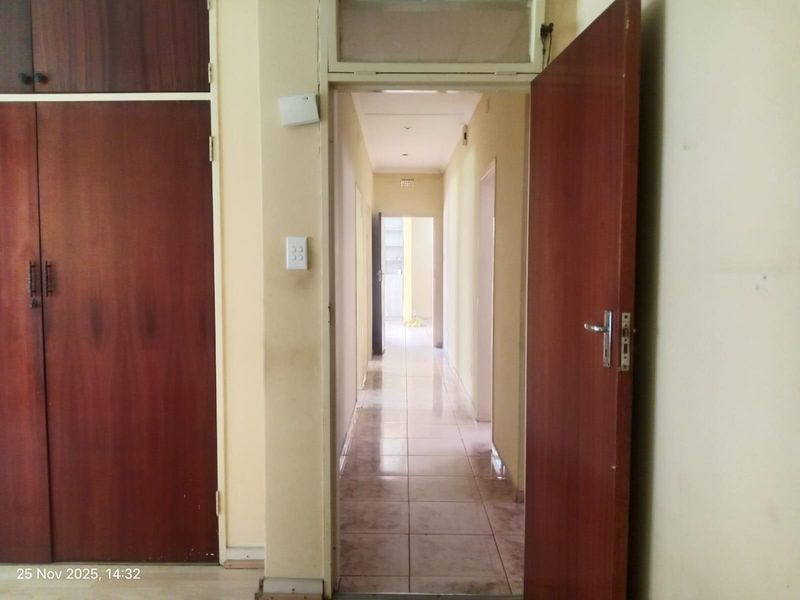 A functional hallway featuring tiled flooring and built-in wooden cupboards, providing access to multiple rooms within the property.