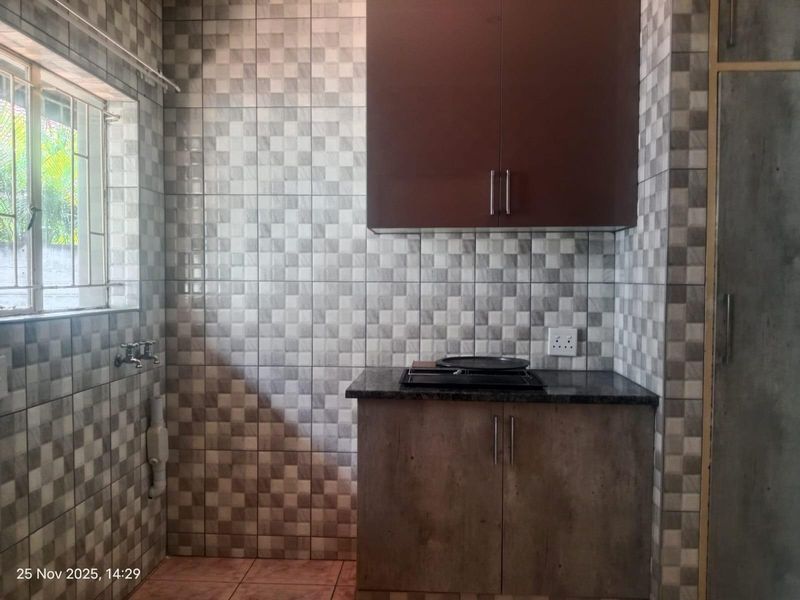 A compact scullery or utility area featuring tiled walls, built-in cabinetry, a granite countertop, and a built-in hob.