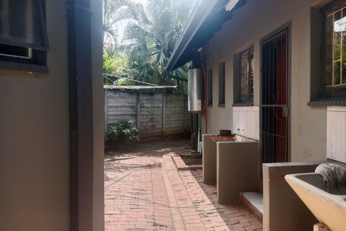 Rear exterior area featuring brick paving, a concrete wash trough, and an external geyser unit against the building wall.