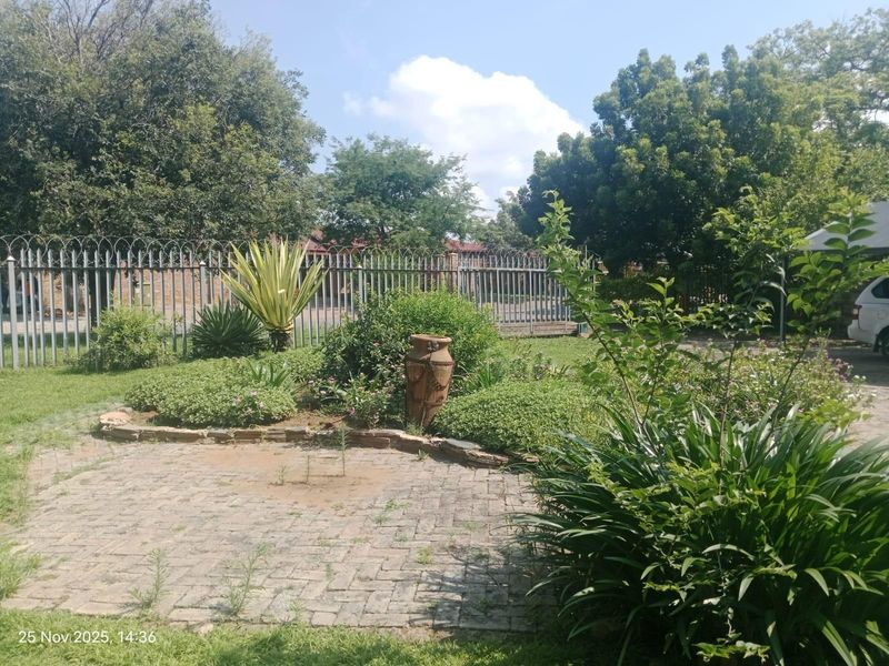 A landscaped garden area featuring a paved patio, established greenery, and secure metal perimeter fencing.
