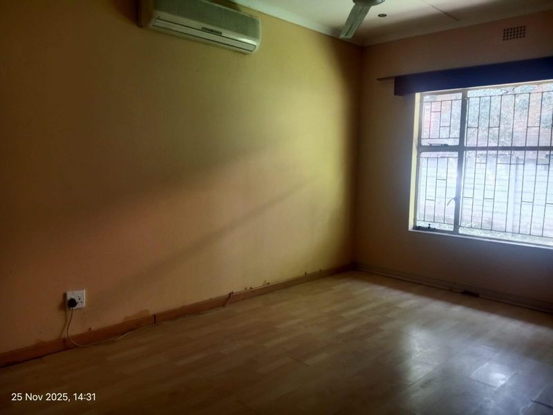 An empty bedroom featuring laminate flooring, a ceiling fan, and a wall-mounted air conditioning unit, with visible signs of wear on the lower walls.