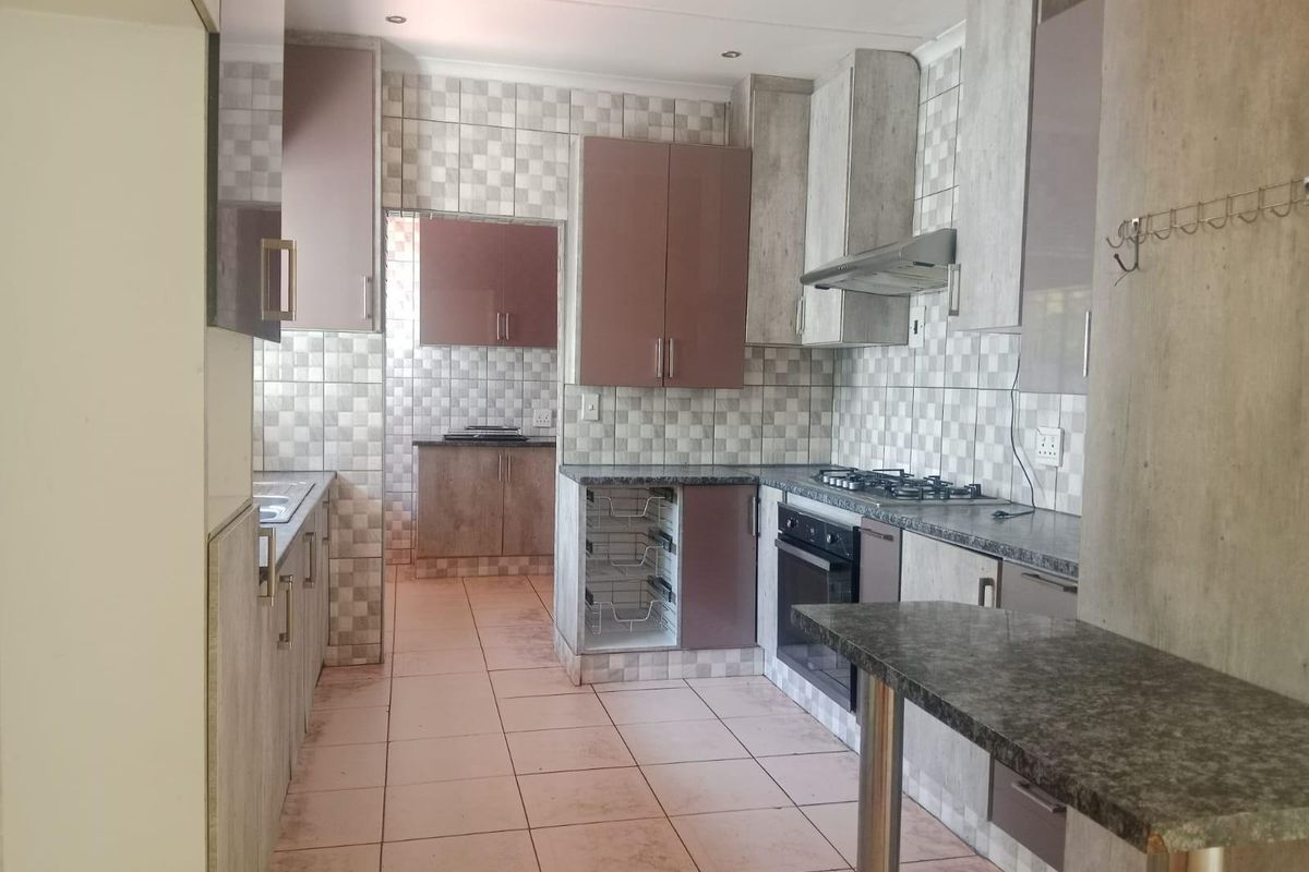 A functional kitchen featuring built-in cabinetry, gas hob, oven, extractor fan, and granite countertops with a breakfast bar area.