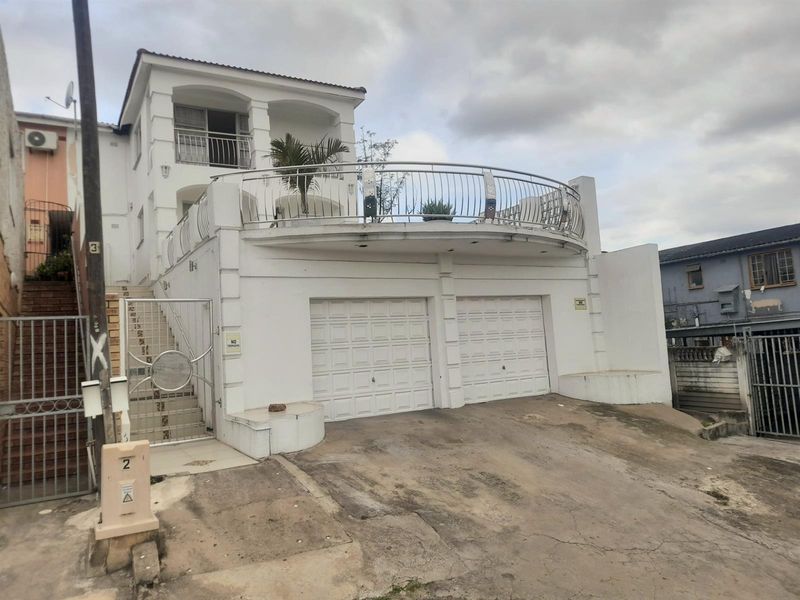 Front elevation of a multi-story house featuring a double garage, an elevated balcony with metal railings, and an external staircase.