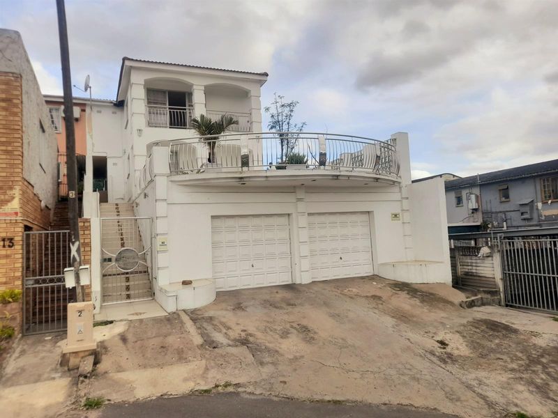 Front elevation of a multi-level house featuring a double garage, a prominent curved balcony with metal railings, and an external staircase.