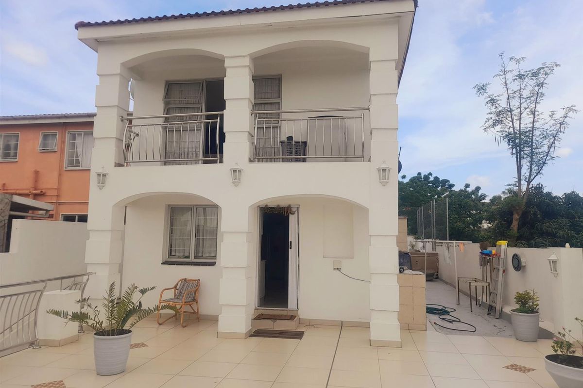 A two-story rear exterior view featuring a tiled patio, a covered balcony with stainless steel balustrades, and classic arched architectural pillars.