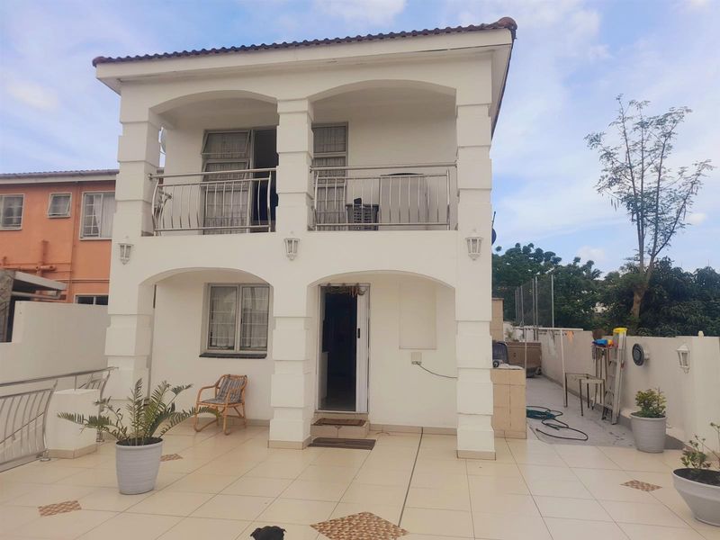 A two-story rear exterior view featuring a tiled patio, a covered balcony with stainless steel balustrades, and classic arched architectural pillars.