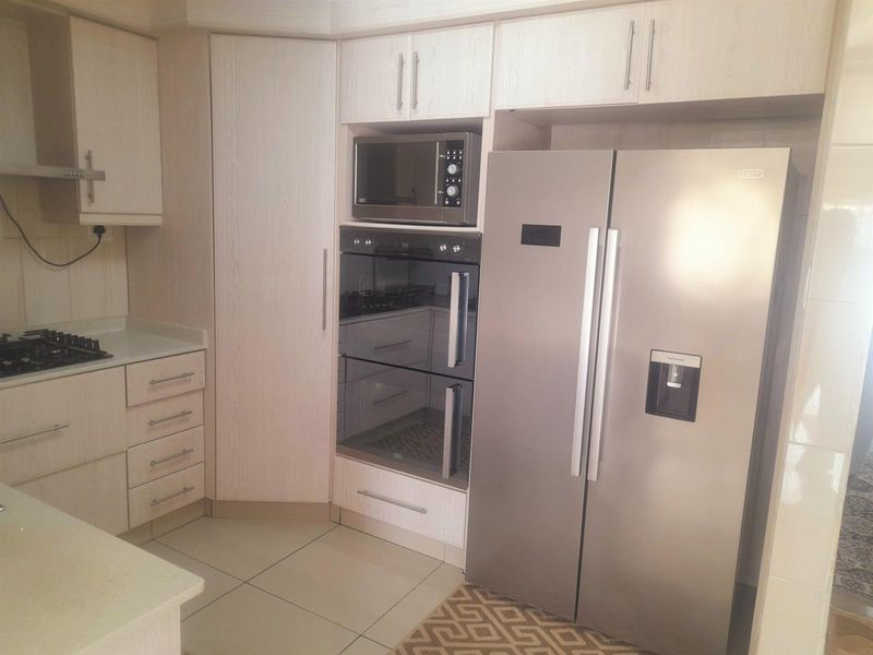 Modern kitchen featuring light wood-finish cabinetry, stone countertops, integrated oven, microwave, and gas hob with tiled flooring.