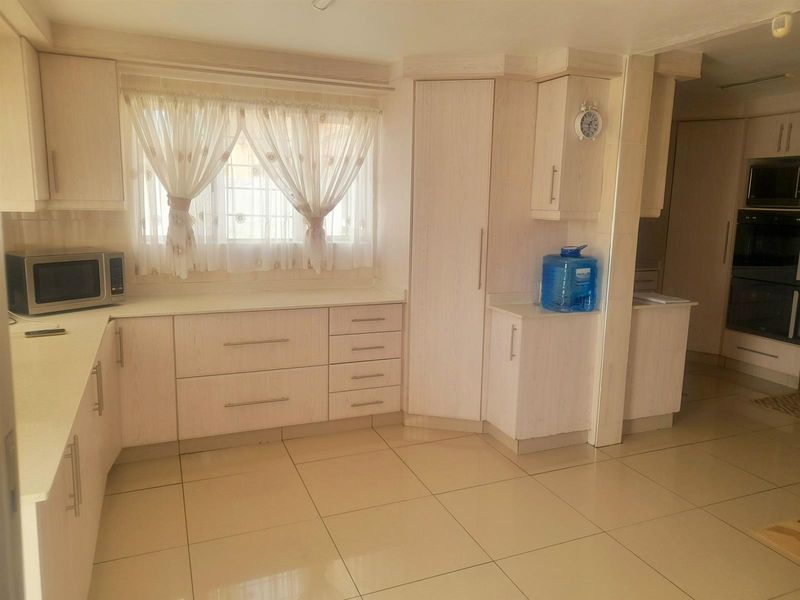 A functional kitchen featuring light-toned built-in cabinetry, tiled flooring, and integrated appliances, offering a clean and practical workspace.