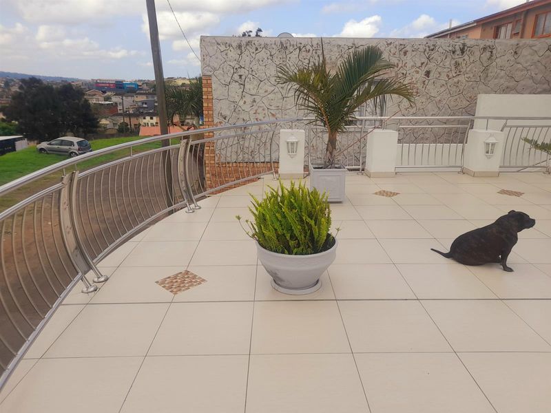 Spacious balcony featuring tiled flooring, a modern stainless steel balustrade, and a decorative stone-clad feature wall with elevated neighbourhood views.