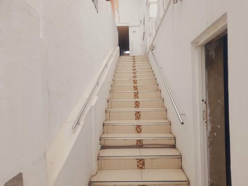 An exterior-facing staircase featuring tiled steps with decorative inserts and stainless steel handrails, showing signs of wear and requiring maintenance.
