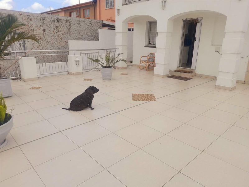 A spacious, tiled outdoor patio area featuring arched architectural pillars, metal balustrades, and exterior wall lighting, providing a clean and functional entertainment space.