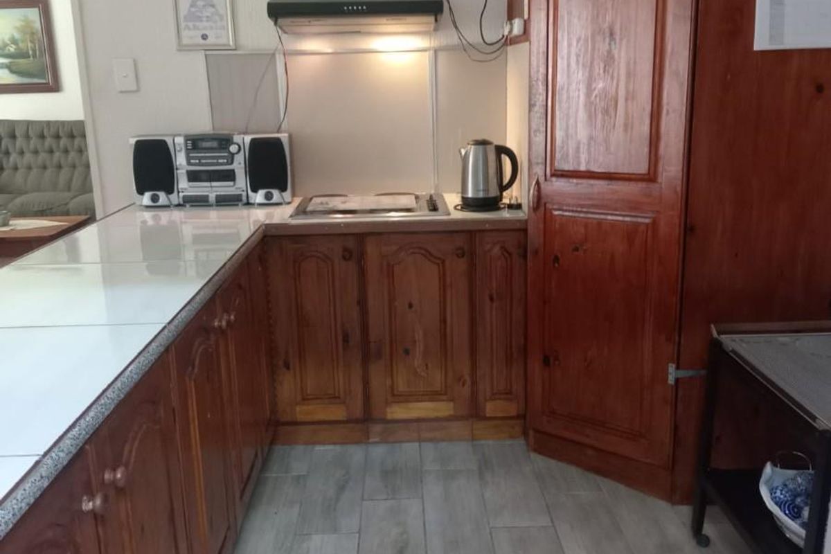 A functional kitchen featuring wooden cabinetry, a built-in extractor fan, a hob, and modern wood-look floor tiles.