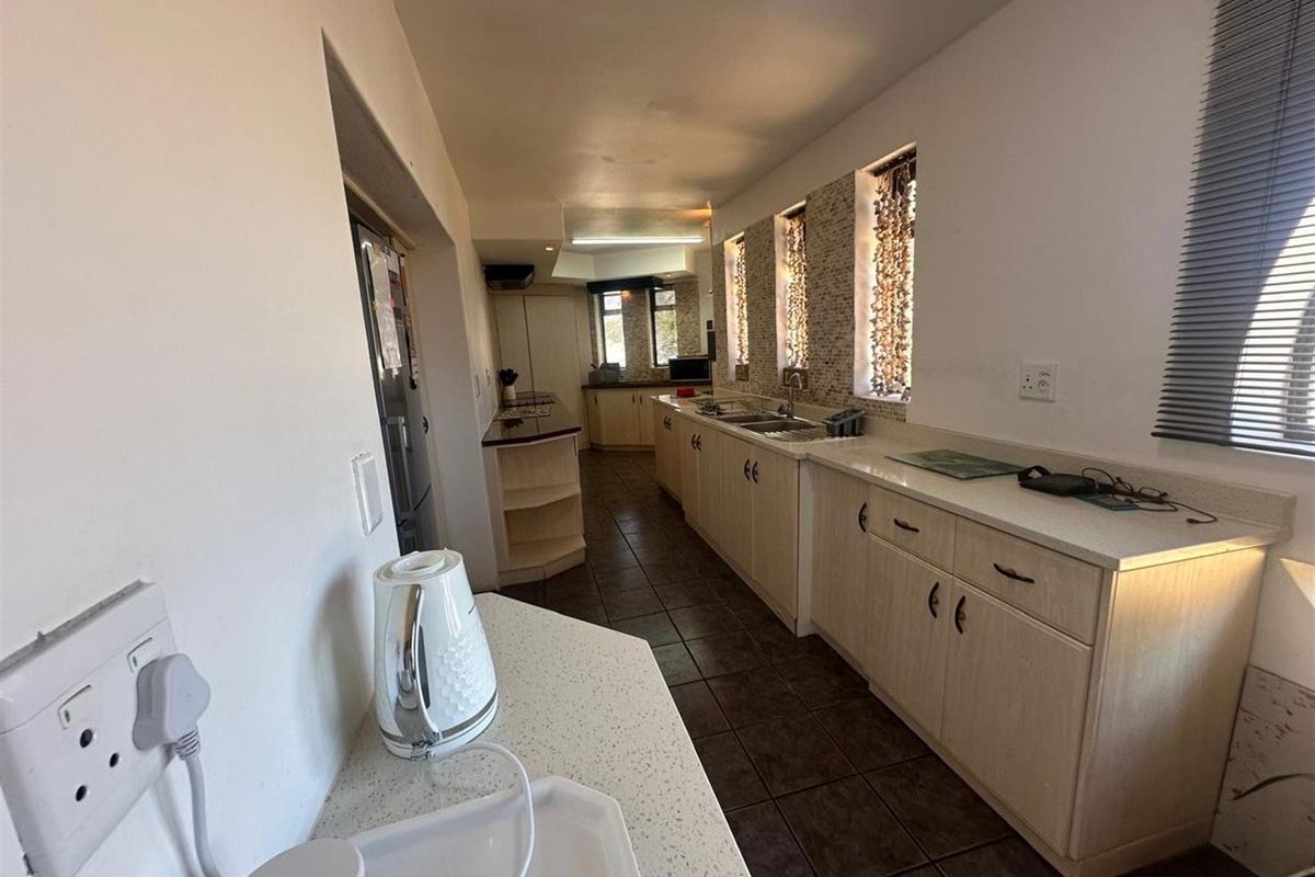 A functional galley-style kitchen featuring light-toned cabinetry, stone-look countertops, tiled flooring, and multiple windows providing natural light.
