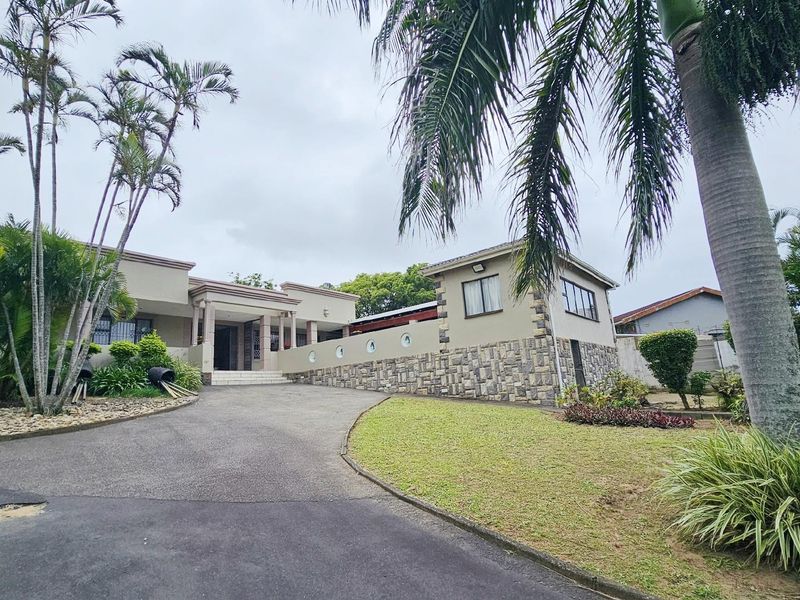 Front elevation of a residential property featuring a paved driveway, stone-clad exterior walls, and established garden landscaping.