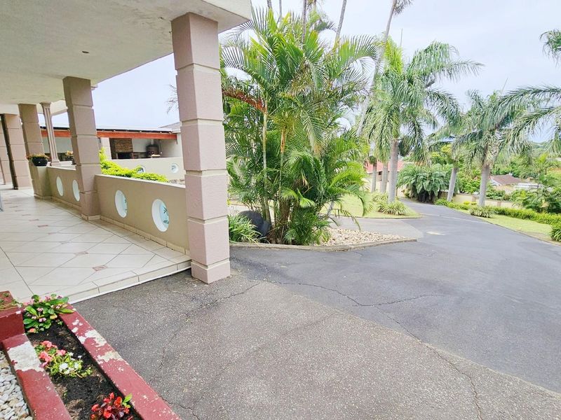 A view of the front entrance featuring a covered tiled patio, concrete columns, and a paved driveway leading to the property.