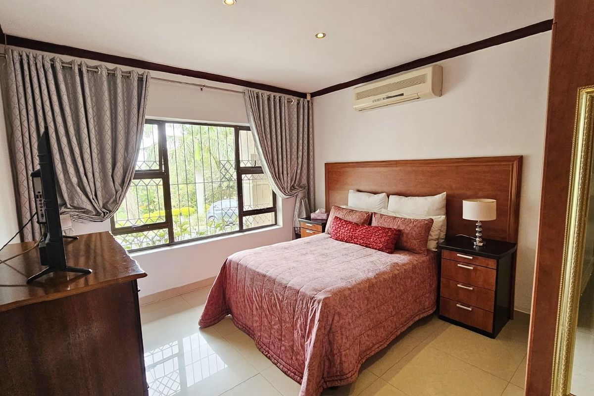 A well-maintained bedroom featuring tiled flooring, a built-in wooden headboard, and a wall-mounted split-system air conditioner.