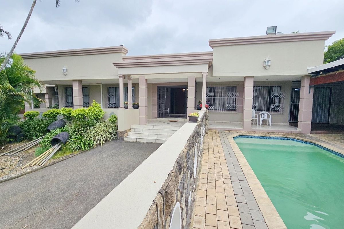 Rear exterior view featuring a swimming pool, paved deck, and a covered patio area with stone-clad retaining wall.