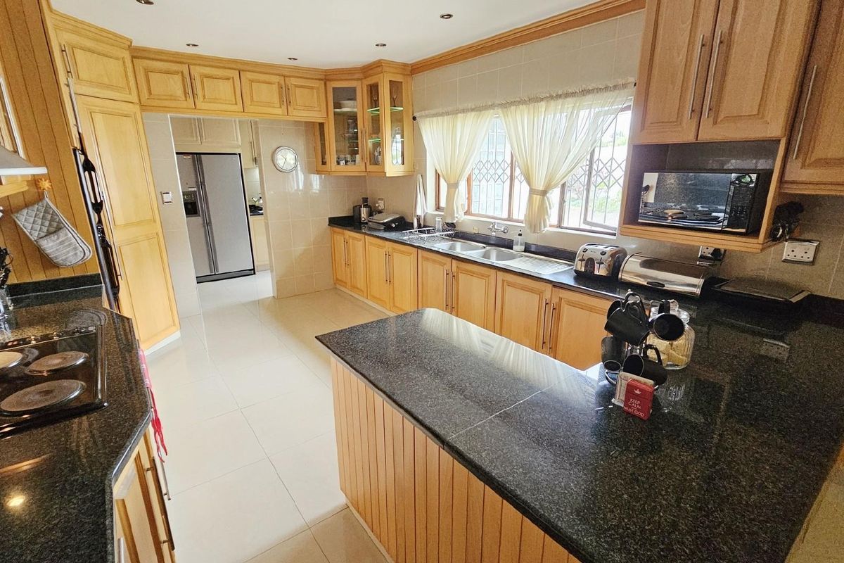 A spacious kitchen featuring light wood cabinetry, dark granite countertops, a double sink, and integrated appliances with a functional layout.