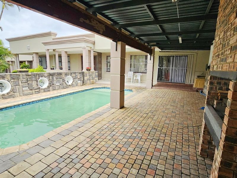 Outdoor entertainment area featuring a swimming pool, covered patio with paved flooring, and a built-in brick braai facility.