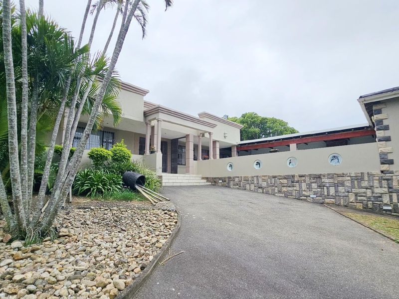 Front elevation of the house featuring a paved driveway, stone cladding accents, and a covered entrance area with decorative wall features.