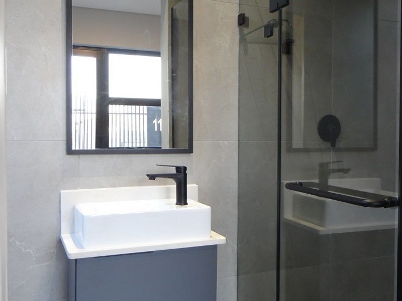 Modern bathroom featuring a wall-mounted vanity with vessel sink, black fixtures, and a glass-enclosed shower with large format grey wall tiles.