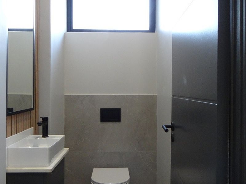 A modern, minimalist guest bathroom featuring a wall-mounted toilet, sleek vanity with vessel sink, and stylish timber slat wall detailing.