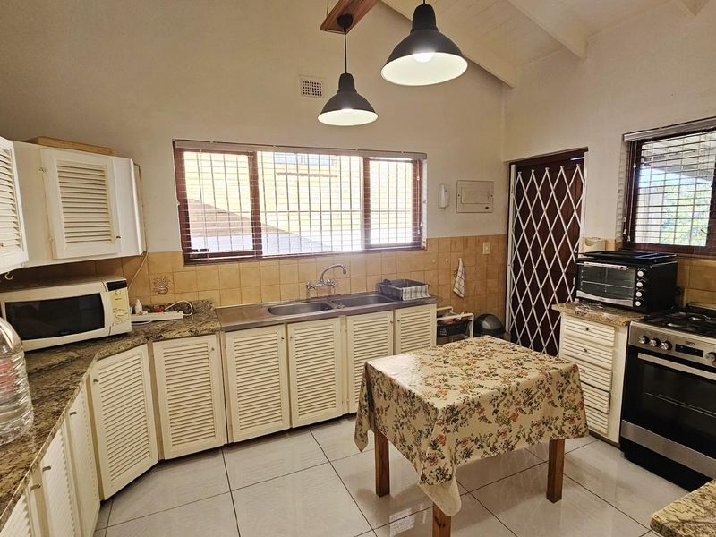 A functional kitchen featuring louvered cabinetry, granite countertops, a double sink, and a built-in gas stove with an extractor fan.