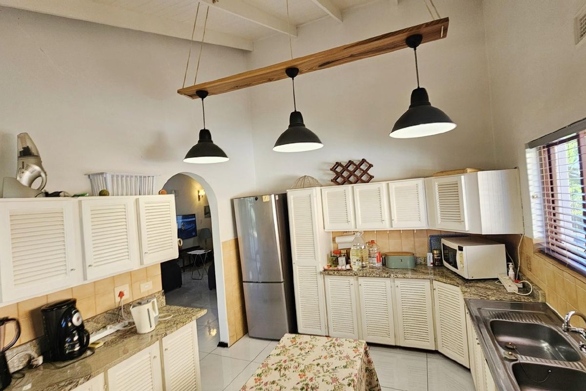 A functional kitchen featuring white louvered cabinetry, granite countertops, a double basin sink, and a distinctive wooden pendant light fixture.
