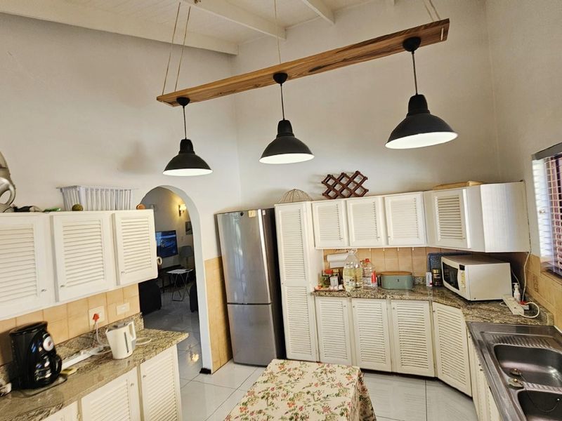 A functional kitchen featuring white louvered cabinetry, granite countertops, a double basin sink, and a distinctive wooden pendant light fixture.