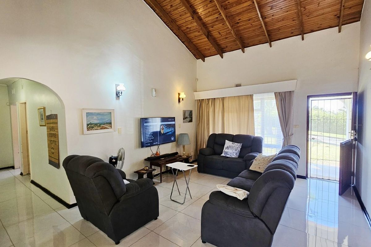 Spacious living room featuring high vaulted timber ceilings, tiled flooring, and direct access to the exterior through a security gate.