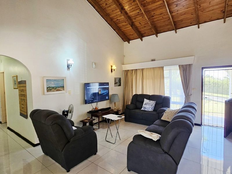 Spacious living room featuring high vaulted timber ceilings, tiled flooring, and direct access to the exterior through a security gate.
