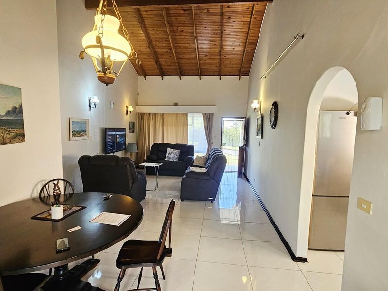 Open-plan living and dining area featuring high vaulted timber ceilings, polished floor tiles, and an arched entryway leading to the kitchen.
