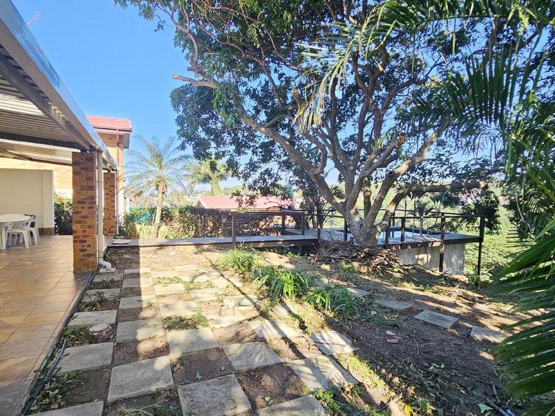 A spacious covered patio area overlooking a garden with mature trees and a raised timber deck, offering potential for outdoor entertainment.