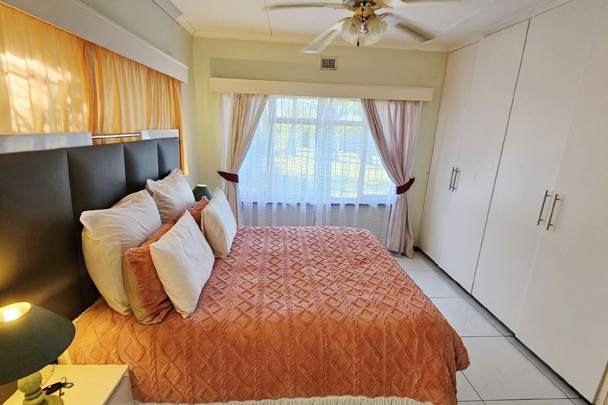A well-lit bedroom featuring built-in floor-to-ceiling wardrobes, tiled flooring, and a ceiling fan, offering a functional and comfortable living space.