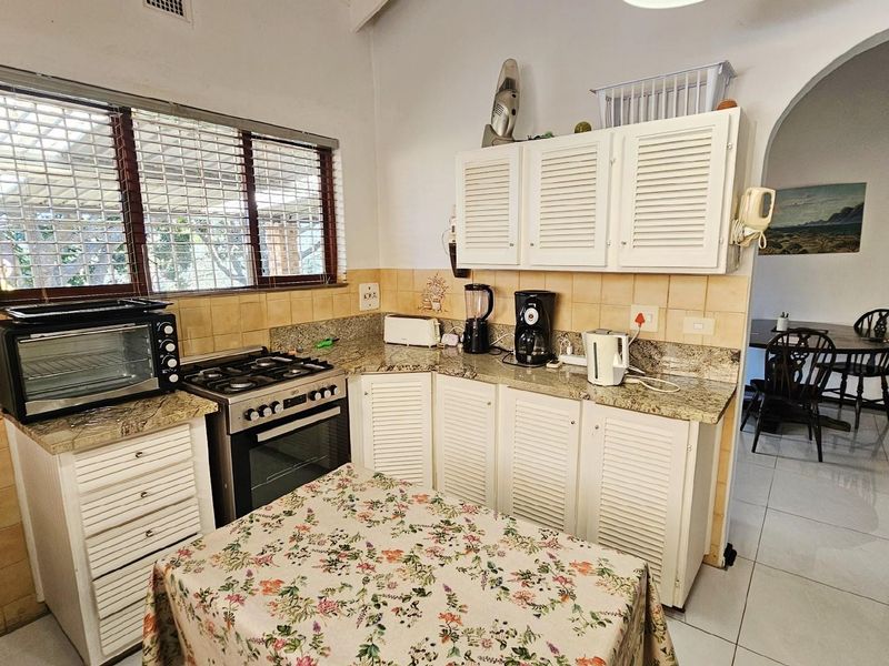 A functional kitchen featuring white louvered cabinetry, granite countertops, a gas stove, and a tiled backsplash, with an adjacent dining area visible.