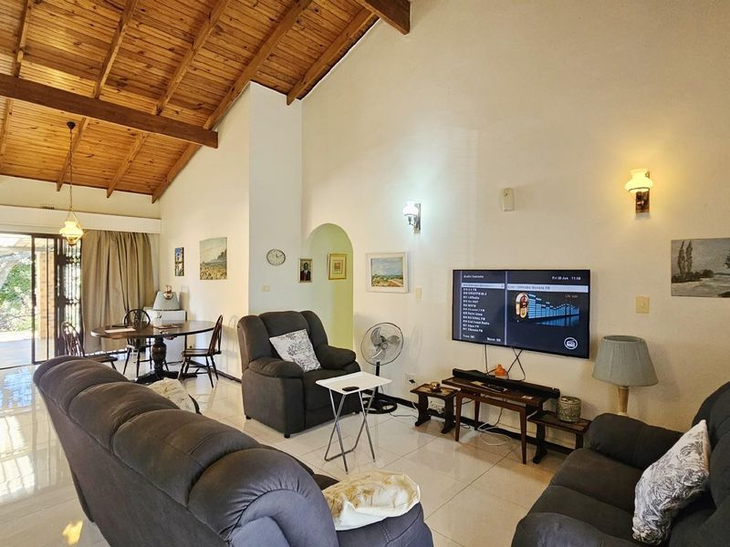 Spacious open-plan living area featuring high vaulted timber ceilings, tiled flooring, and sliding glass doors leading to an outdoor patio space.