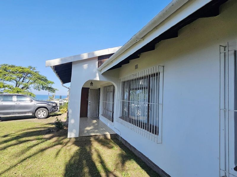 Side exterior view of the house featuring a covered entrance, security bars on windows, and a surrounding lawn area.
