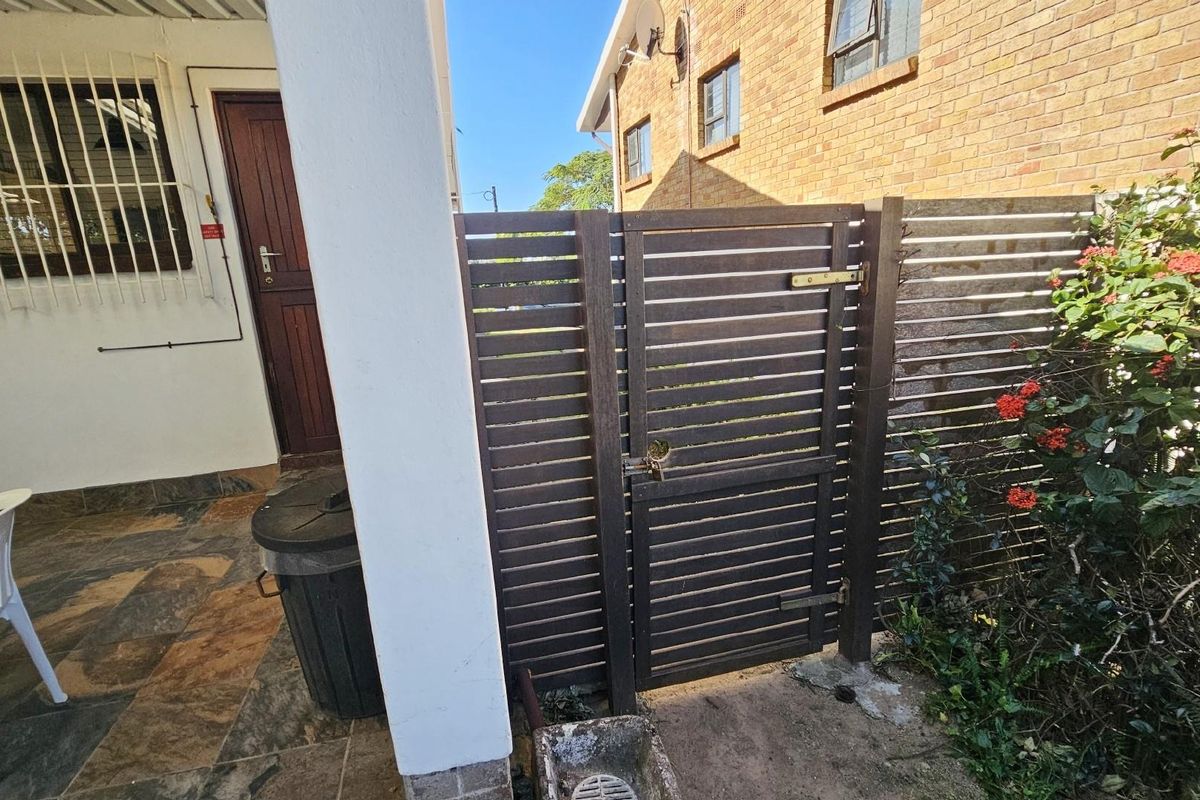 A side access area featuring a slatted timber gate, tiled patio flooring, and brick exterior walling, providing secure entry to the rear of the property.
