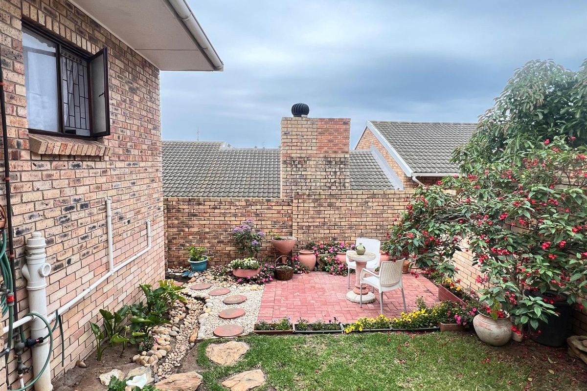 A private rear courtyard featuring a brick-paved patio area, established garden beds, and a brick boundary wall, providing a quiet outdoor space.
