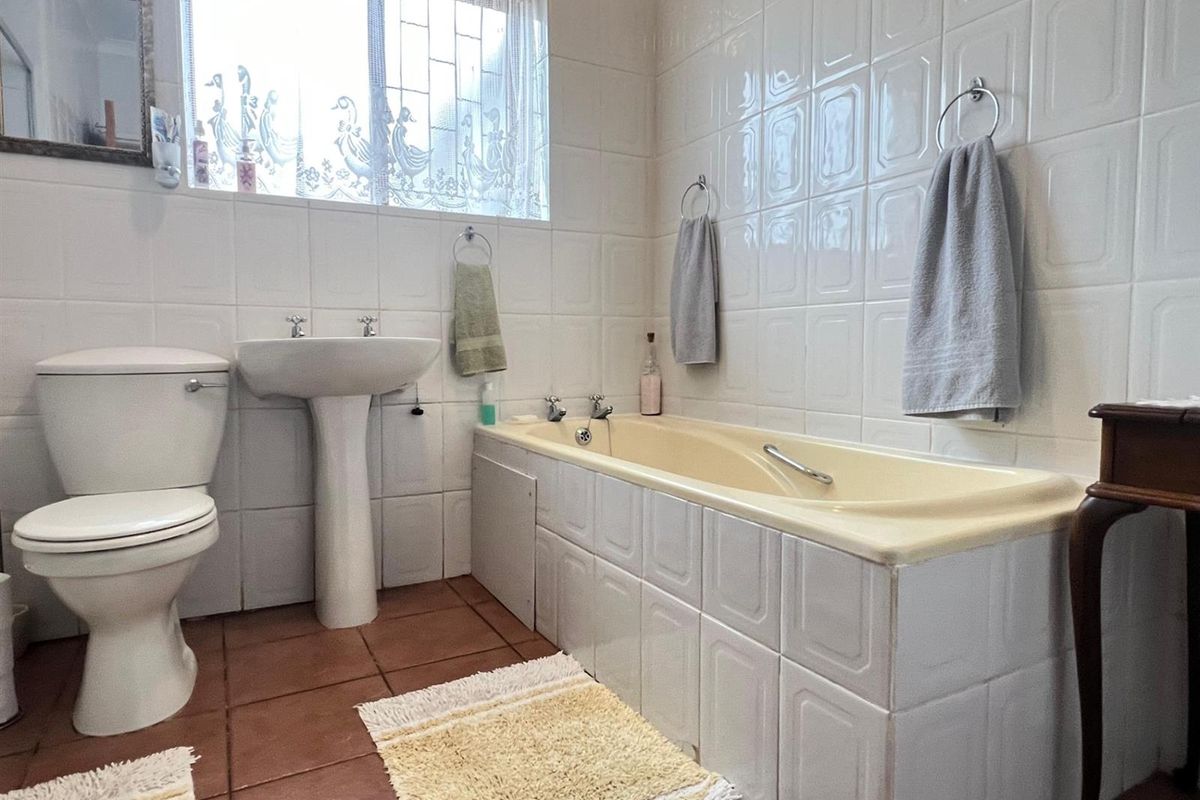A functional bathroom featuring a pedestal basin, a toilet, and a built-in bathtub with tiled surround and terracotta floor tiles.