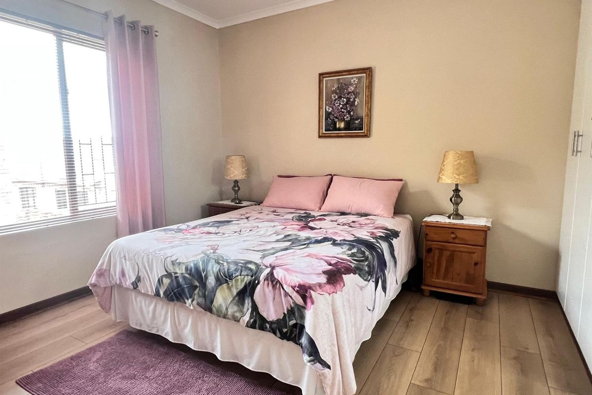 A well-maintained bedroom featuring light wood-look laminate flooring, built-in cupboards, and a large window allowing for natural light.