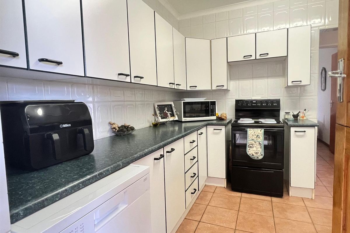 A functional kitchen featuring white cabinetry, dark laminate countertops, tiled splashbacks, and tiled flooring, equipped with a freestanding stove.