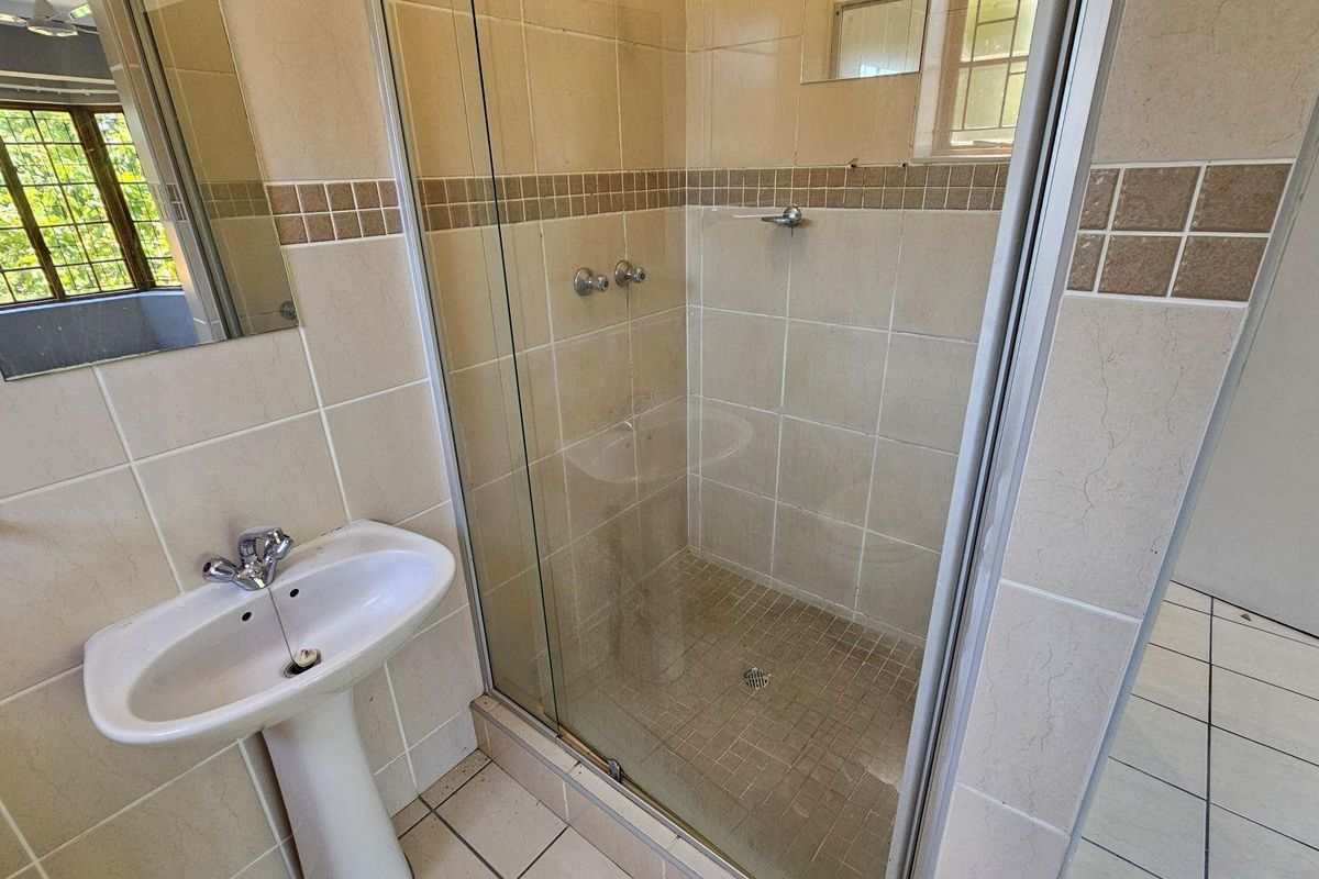 A functional bathroom featuring a pedestal basin, a glass-enclosed shower, and neutral wall tiling.