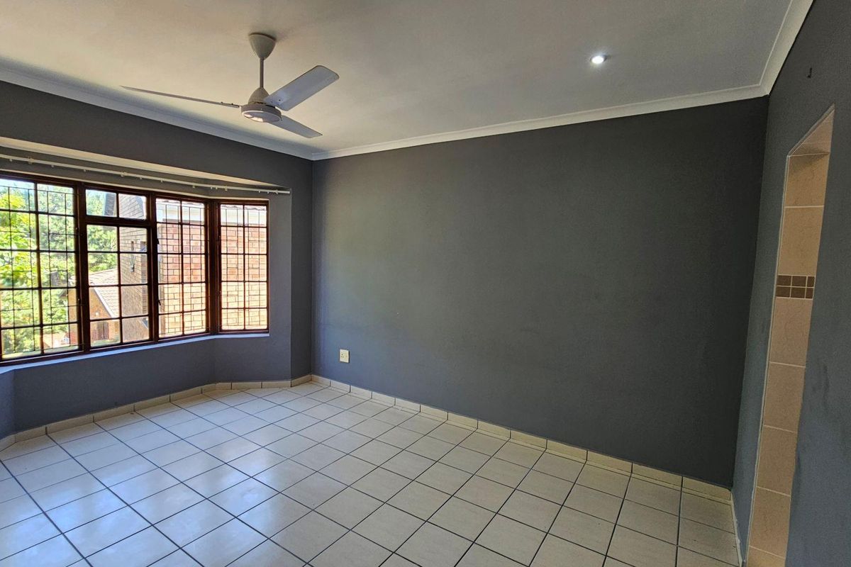 A spacious, empty bedroom featuring tiled flooring, a ceiling fan, and a large bay window providing natural light.