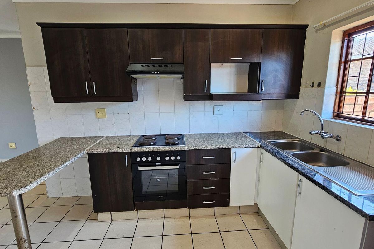 A functional kitchen featuring dark wood cabinetry, granite-look countertops, a built-in oven with hob, extractor fan, and a double stainless steel sink.