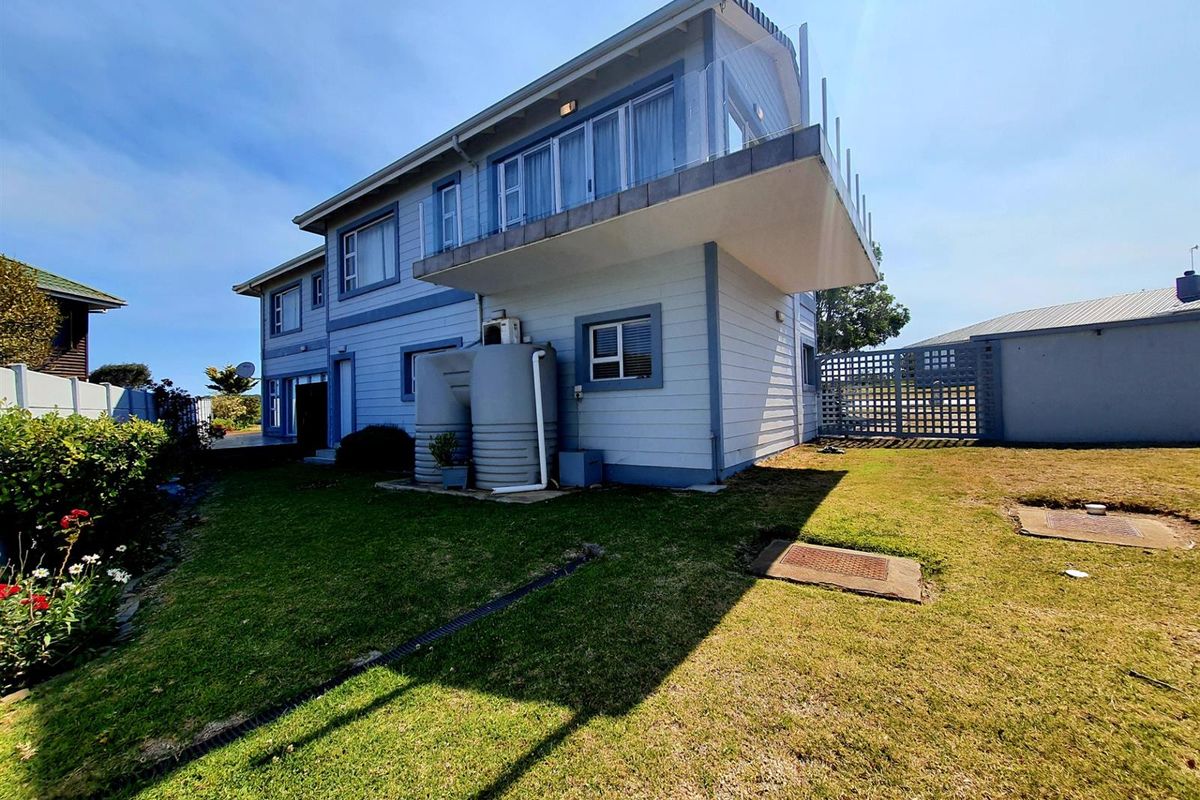 Rear view of the two-story house featuring a cantilevered balcony, exterior cladding, and a private garden with water storage tanks.