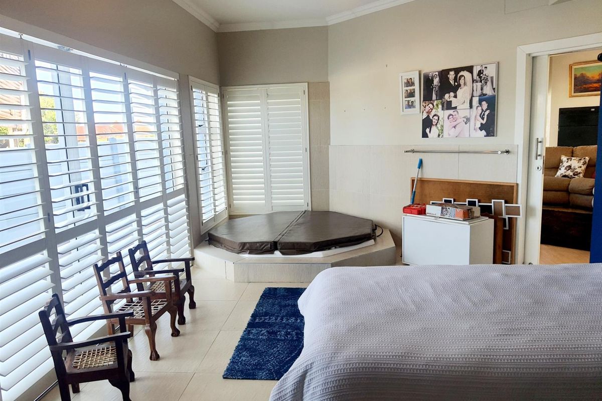 Spacious bedroom featuring a built-in corner spa bath, tiled flooring, and white plantation shutters providing ample natural light.