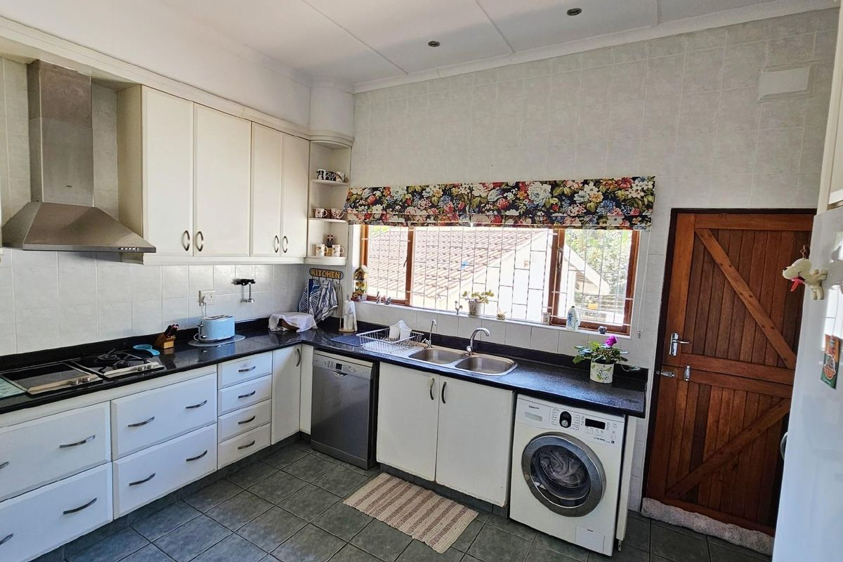 A functional kitchen featuring white cabinetry, dark countertops, a stainless steel extractor fan, double sink, and integrated laundry appliance space.